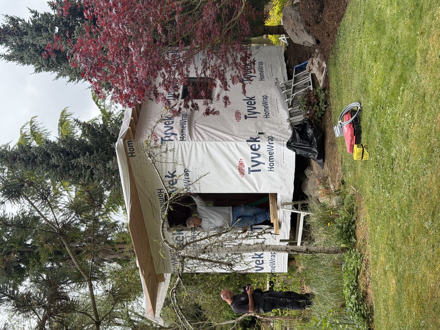 Two Durak Homes crew members at the studio doorway with the roof and weather barrier complete, tools laid out on the lawn.
