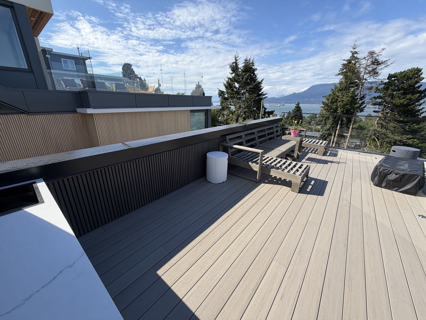 Two-tone composite decking meeting a dark slatted screen wall and built-in bench, with a stone counter in the foreground.