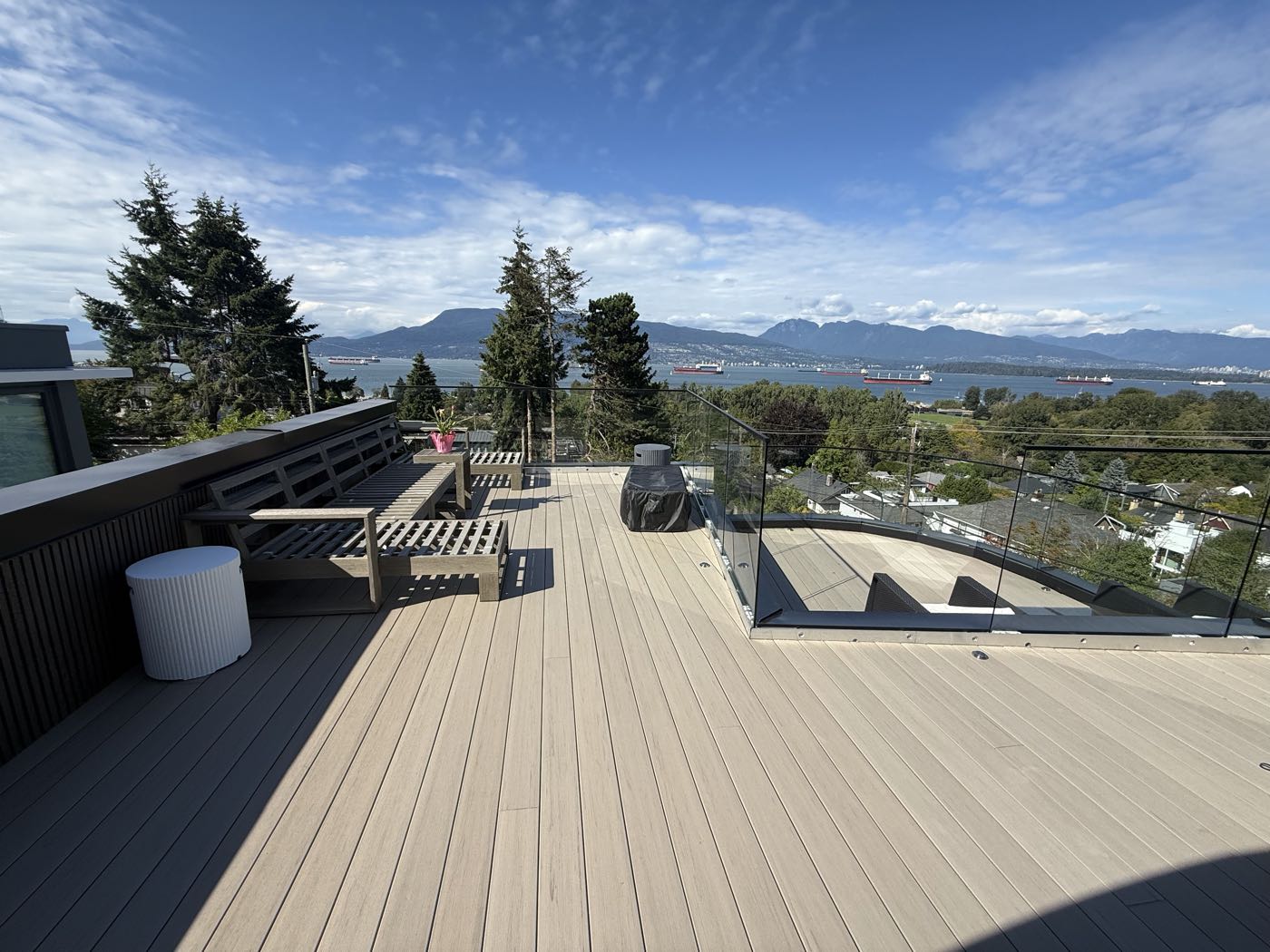 The same roof deck from the upper level, with the curved lower deck and its glass guard visible beyond, freighters at anchor in English Bay.