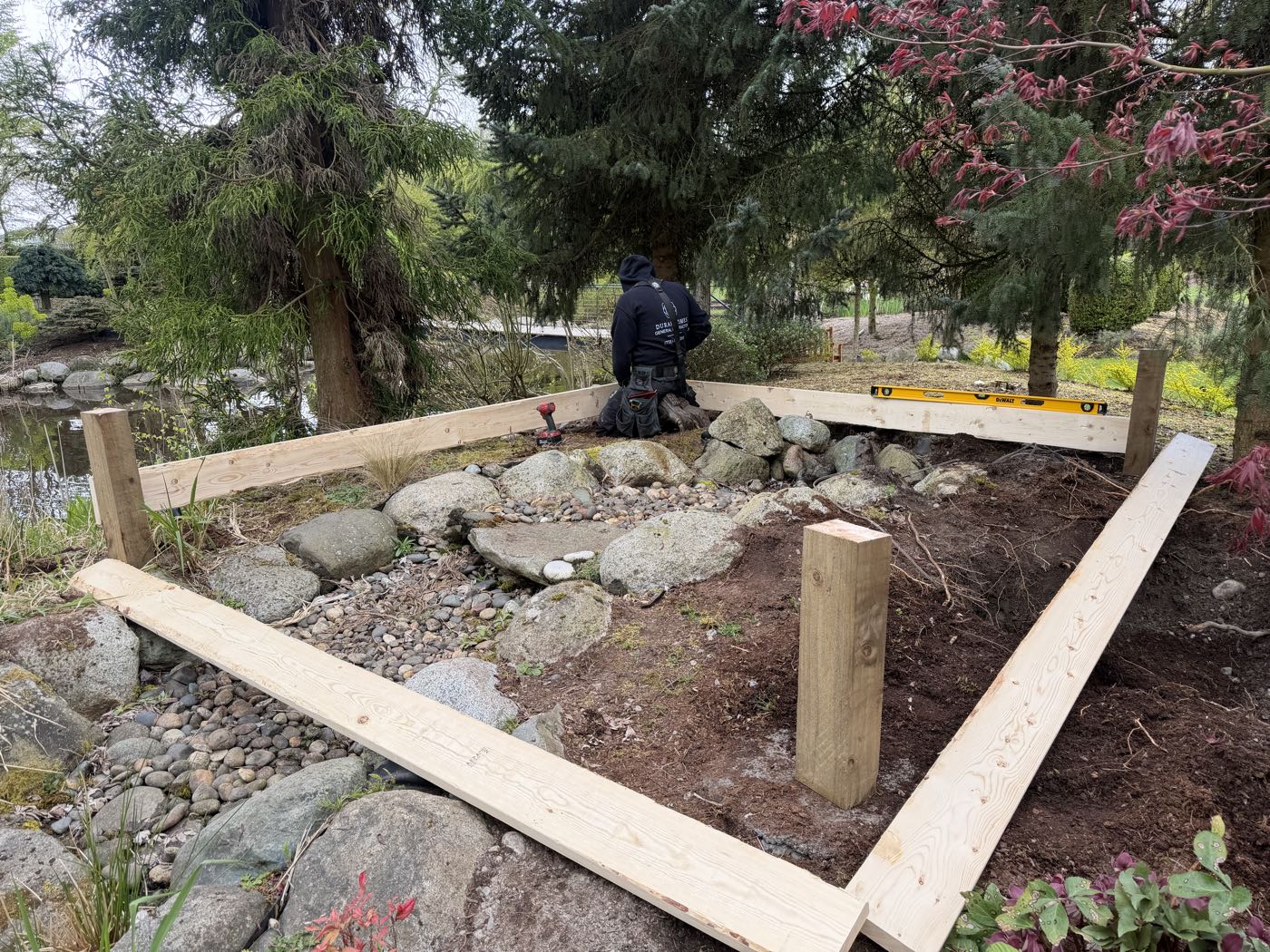 Pressure-treated sill plates laid out and squared on a gravel and stone base, a level resting on the far beam, before the garden studio floor frame goes down.